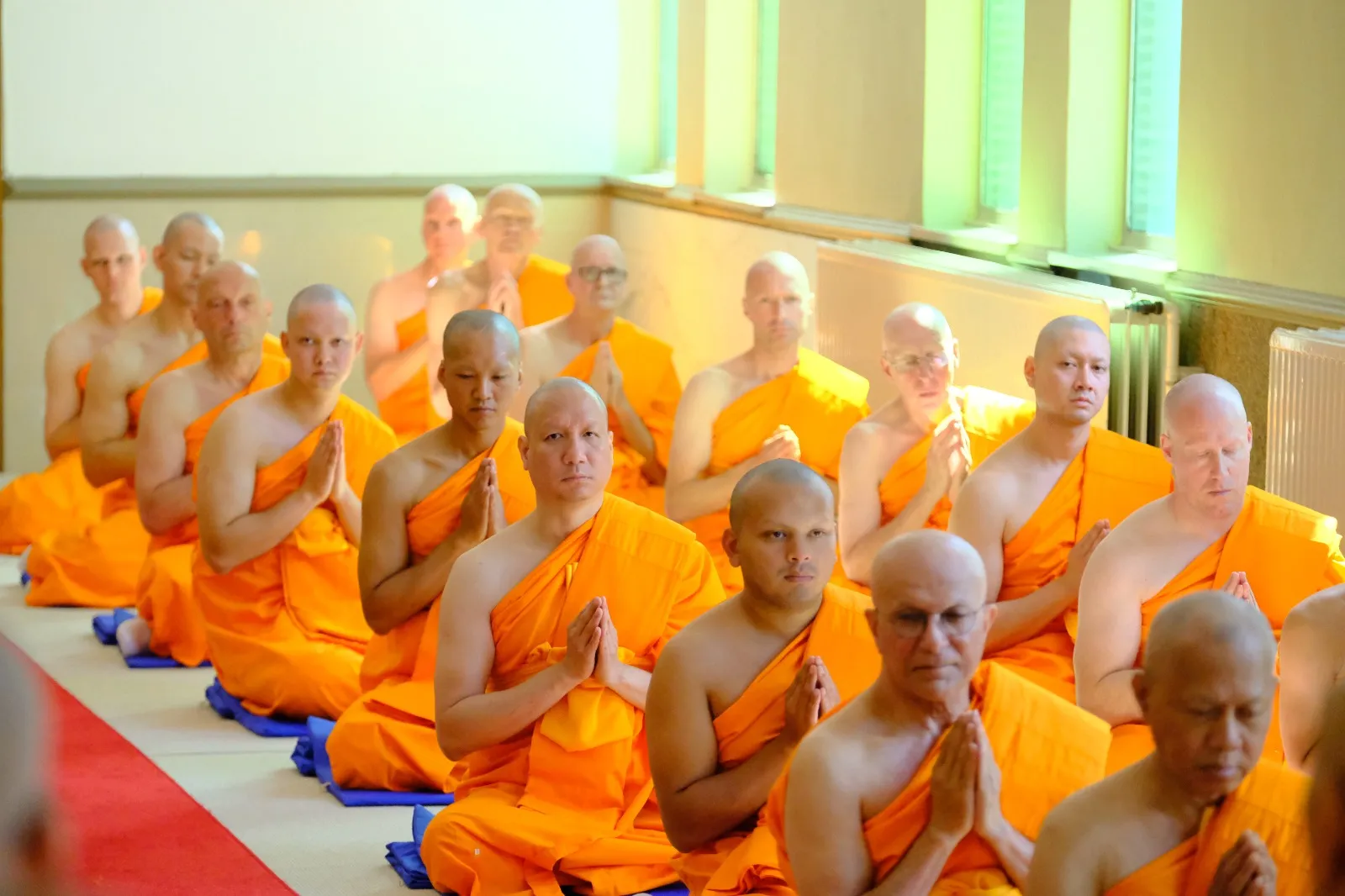 Rows of newly ordained monks kneeling in the hall with palms pressed together